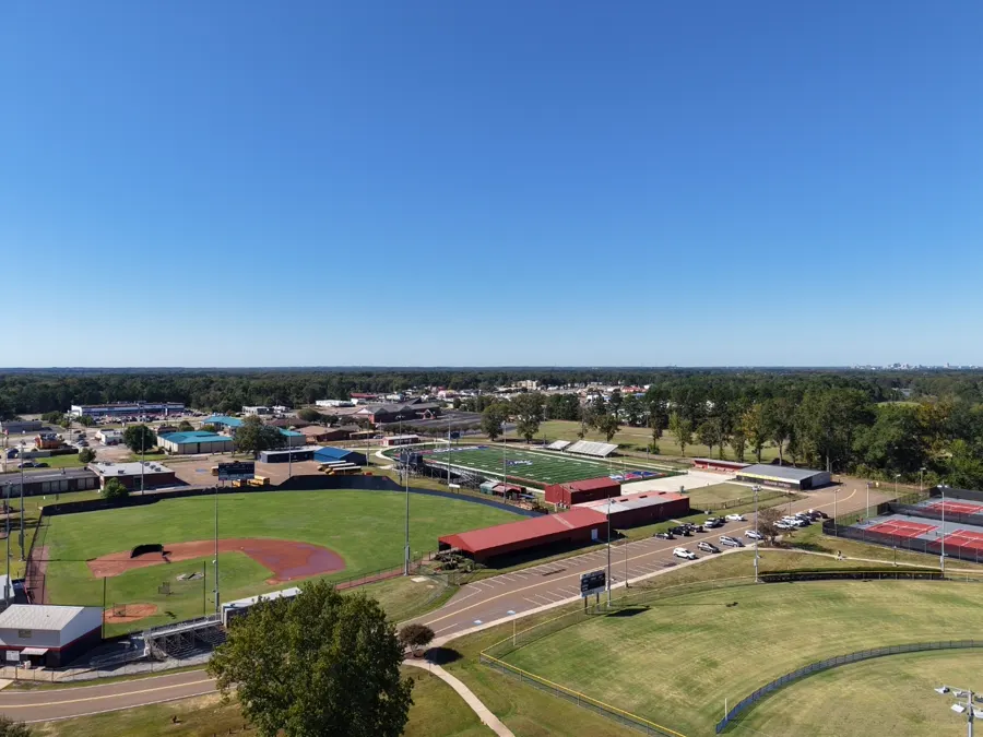 Wide aerial view of a school campus with athletic fields, tennis courts, and parking